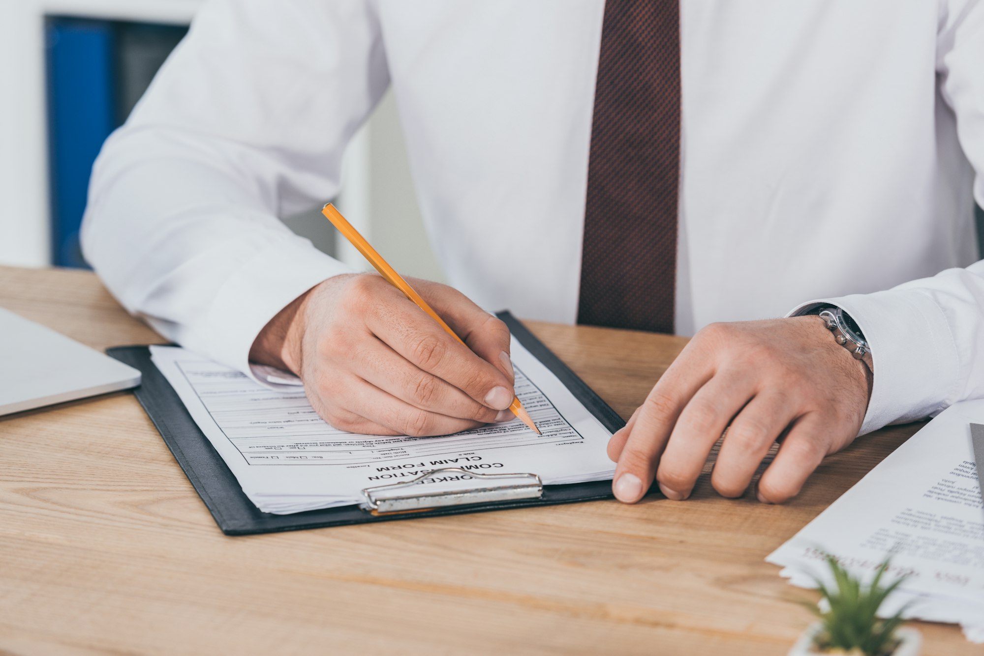 cropped view of businessman writing on compensation claim form at workplace