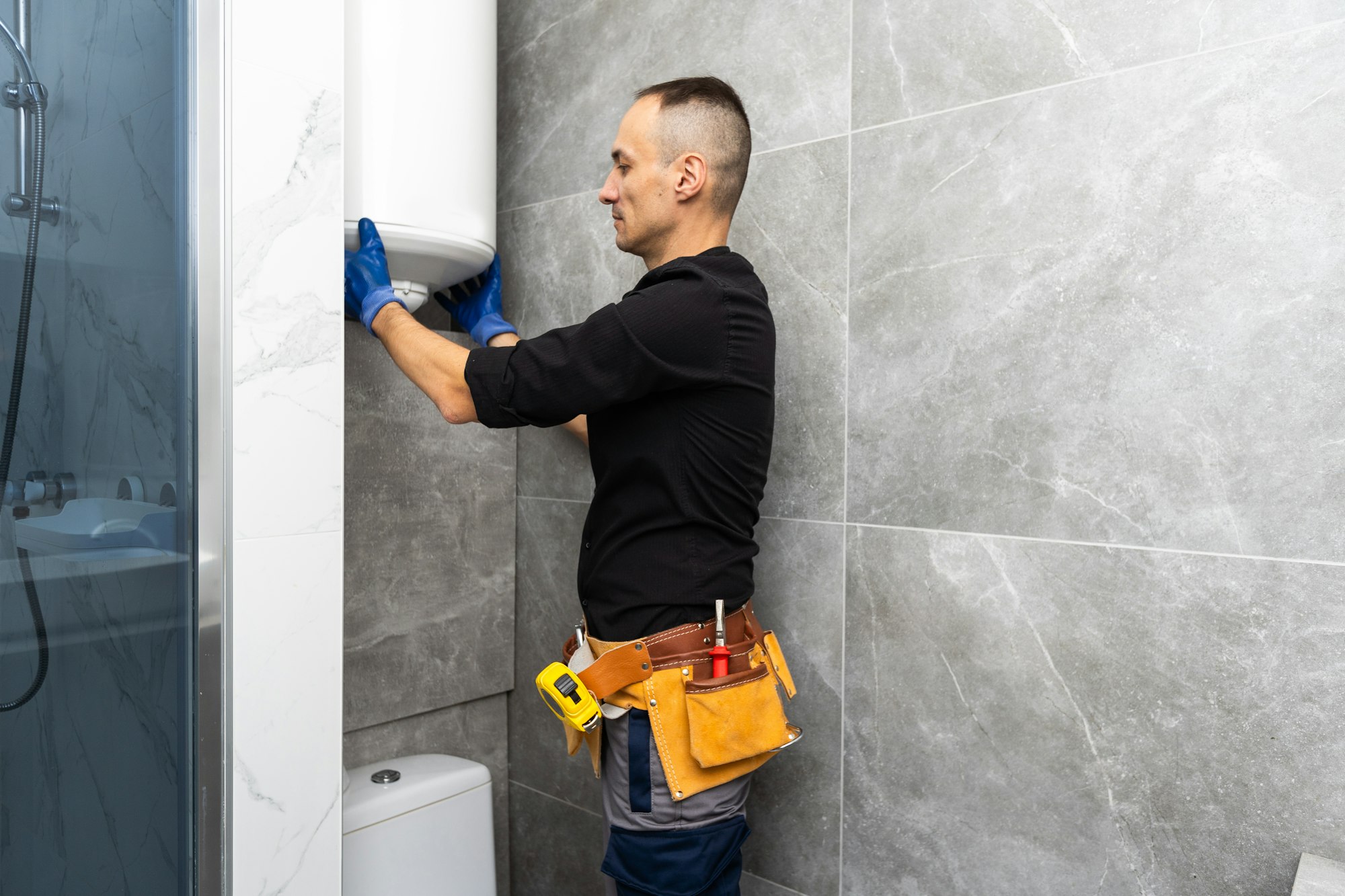 Male plumber repairing boiler in bathroom